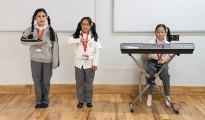 Three Junior School students perform during a classroom music activity, two standing and gesturing rhythmically while one plays an electronic keyboard.